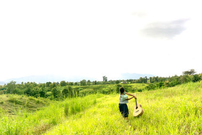 Girl with acoustic guitar standing on grassy field