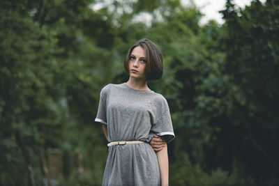 Portrait of beautiful young woman standing against trees