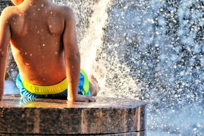 Rear view of shirtless man splashing water