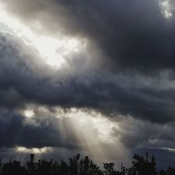 Low angle view of sunlight streaming through clouds