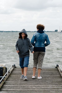 Female friends on jetty by sea against sky