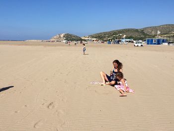 Mother with daughter using phone at sandy beach on sunny day