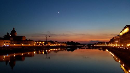 Illuminated buildings by river against sky at night