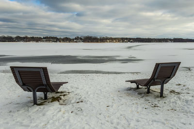 Empty bench on beach against sky during winter