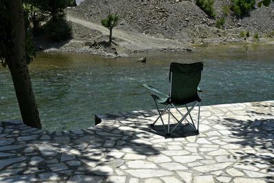 Empty chair by lake against trees