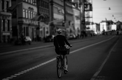 Rear view full length of woman riding bicycle on road in city