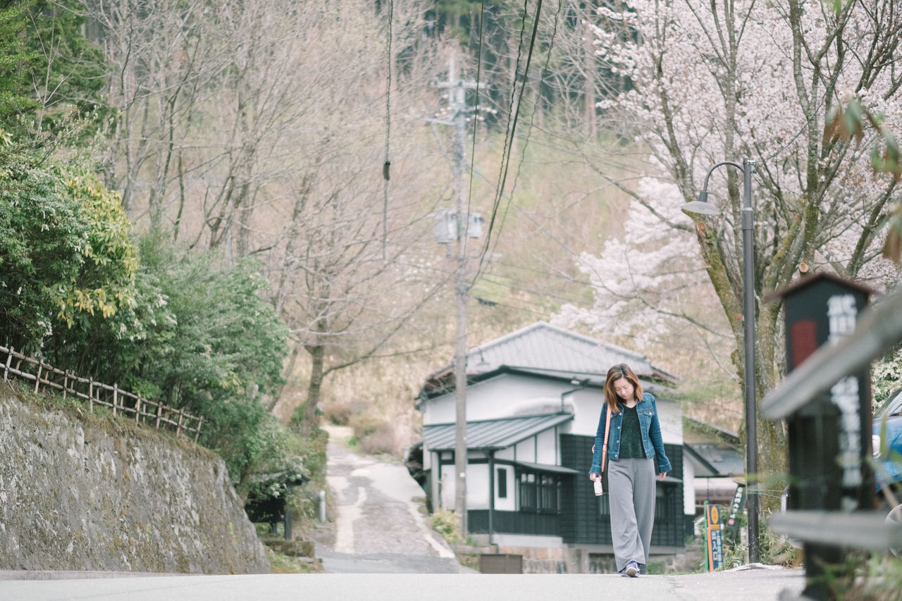 MAN STANDING ON ROAD AMIDST TREES