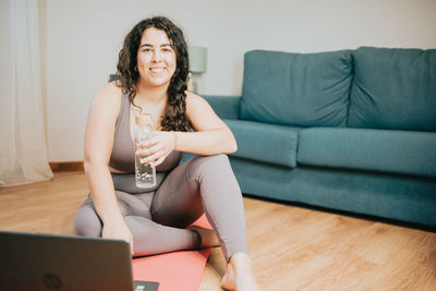 Smiling young woman with water bottle sitting at home