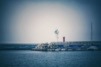 Lighthouse by sea against clear sky