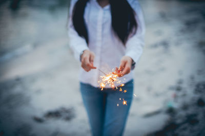 Midsection of woman holding sparkler at night