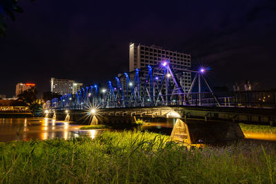 Illuminated bridge over river by buildings in city at night