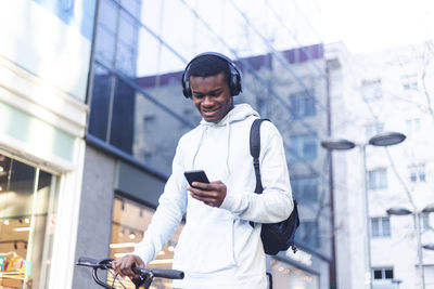 Young man listening to music while using phone outside building