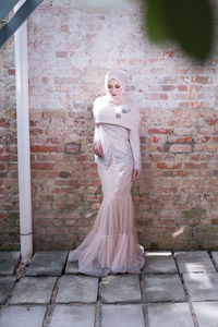 Full length of woman standing against brick wall