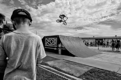 Rear view of boy skateboarding on skateboard against sky