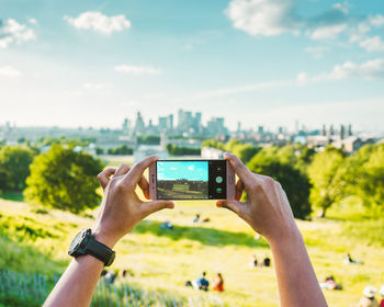 Man photographing with mobile phone against sky