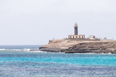 Lighthouse by sea against clear sky