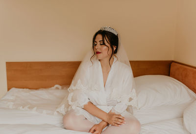 Portrait of young woman sitting on bed at home