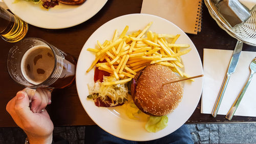 Cropped image of person having burger and beer on restaurant table