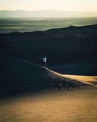 People walking on land against sky during sunset