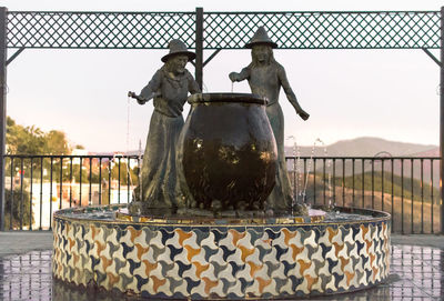 Statue by railing against sky during sunset