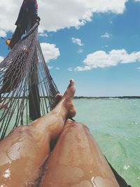 Low section of woman in hammock at beach against sky