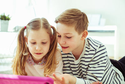 Siblings using digital tablet while lying at home