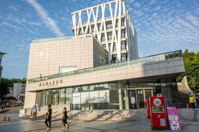 People walking on footpath by building against sky