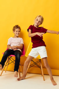 Portrait of smiling young woman sitting against yellow background