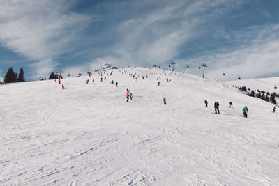 Tourists skiing on snow covered mountain against sky