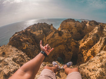 Low section of people on rock by sea against sky