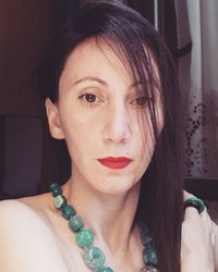 Close-up portrait of woman wearing necklace and red lipstick at home