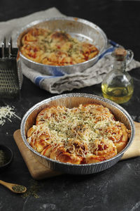 Roll pull apart bread pizza with shredded cheese topping on aluminum foil baking dish