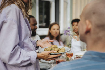 Midsection of woman holding baby potatoes in plates during dinner party at cafe