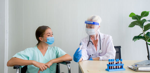 Smiling doctor wearing mask showing thermometer to patient