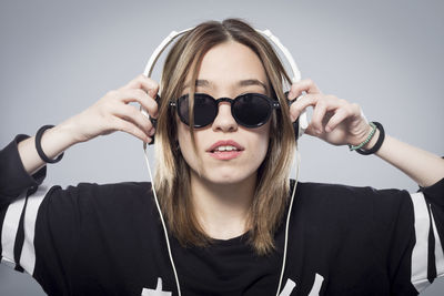 Portrait of young woman listening music on headphones against gray background