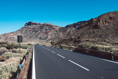 Road leading towards mountains against clear sky