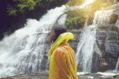 Side view of woman in raincoat standing against waterfall 