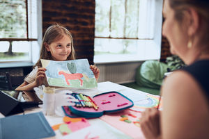 Girl presenting her artwork teacher. woman assisting schoolgirl during classes at primary school