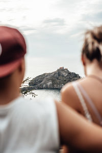 Rear view of couple sitting against rock mountain in sea