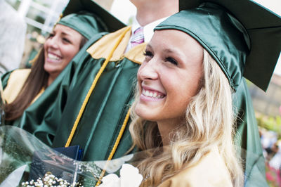 Close-up of happy young woman with friends at graduation ceremony