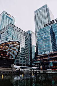 Low angle view of modern buildings by river against sky