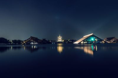 Illuminated city by sea against sky at night