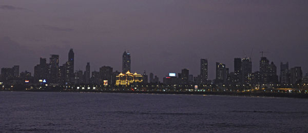 Illuminated buildings by sea against sky at night