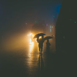 Silhouette of mother and sons walking on road at night during rainy season