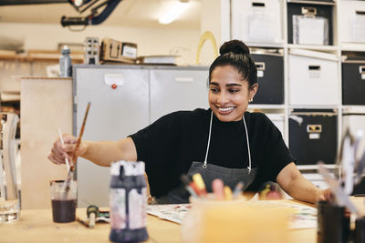 Smiling female student in apron painting at table in art class