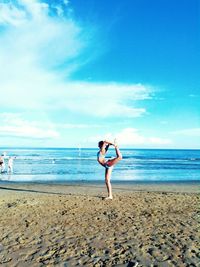 Side view of woman exercising on shore at beach against sky