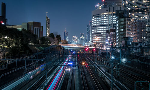 Illuminated railroad tracks amidst buildings in city at night