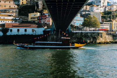 Boat sailing on river below bridge in city