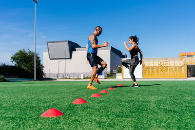 Full body side view of focused sporty man and woman doing lunges while exercising with agility ladder on green grassy lawn on sports ground