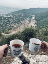 Midsection of woman holding tea cup against mountains